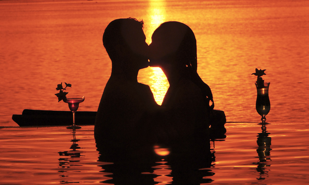 silhouette of couple kissing in a pool at sunset